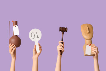 Female hands with auction paddle, gavel and antique items on lilac background