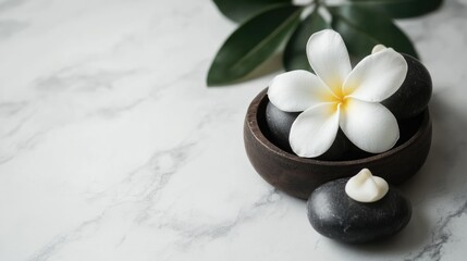 Spa treatment setup with smooth black stones, a white flower, and green leaves on a light marble surface with Copy Space
