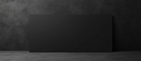 Black blank rectangular panel against a dark textured wall in an indoor setting with ample copy space for text insertion