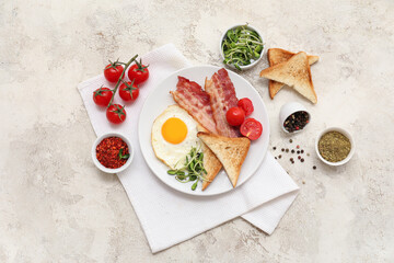 Plate with tasty fried egg, bacon, toasts, tomatoes and spices in bowls on white grunge background. Top view