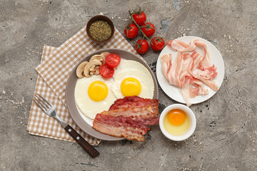 Plate with fried eggs, bacon, mushrooms and tomatoes on grey background. Top view
