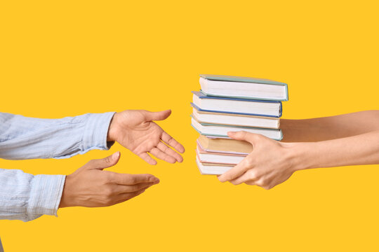 Female hands passing stack of books to another person on yellow background