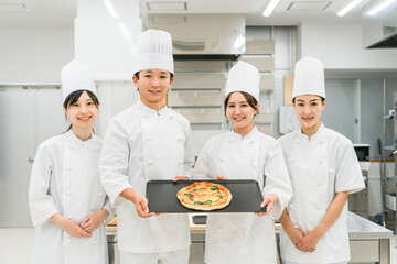 厨房・キッチンに立つコックコート姿の調理師・シェフ・コックの男女
