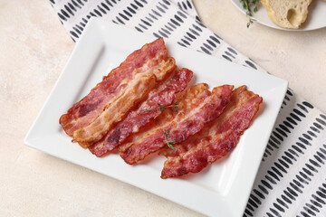 Plate with slices of fried tasty bacon on napkin on white background. Top view
