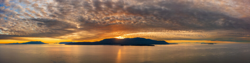 Dramatic and colorful sunset over Orcas Island in the San Juan Islands archipelago of Washington State. Aerial drone view of an amazing cloudscape as seen from Lummi Island located in the Salish Sea.