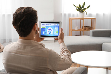 Young man with smart home security system control panel in room, back view