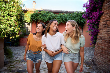 Fantastic time spent with best friends. Three happy girls having fun outdoors in summer vacations at city. Portrait of smiling woman hugging Walking arm in arm together. Female Tourist holidays 