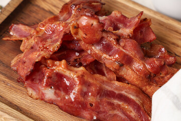 Wooden board with fried bacon rashers on white background, closeup