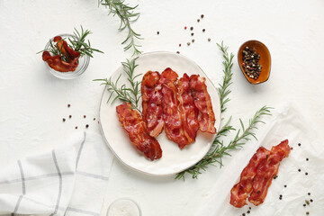 Plate with fried bacon rashers, rosemary and bowl of peppercorn on white background