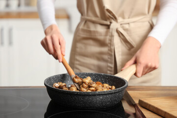 Woman frying mushrooms on electric stove in kitchen, closeup