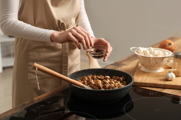 Woman peppering roasted mushrooms in kitchen, closeup