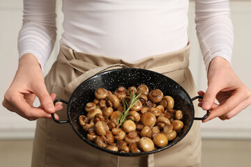 Woman holding frying pan with roasted mushrooms in kitchen, closeup