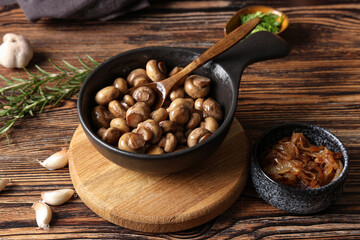 Frying pan with roasted mushrooms and bowl of onion on wooden background