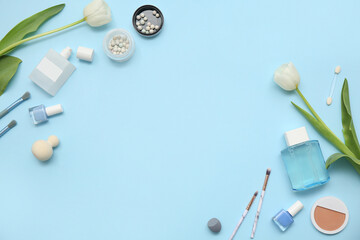Frame made of makeup products, accessories, bottles of perfume and flowers on blue background