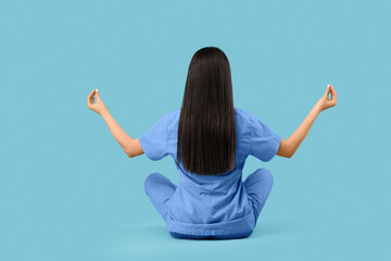 Young female doctor meditating on blue background, back view
