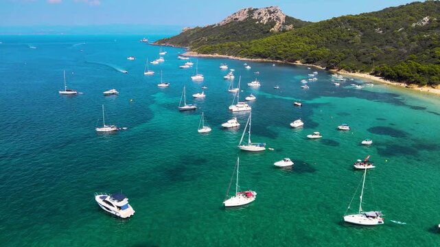 Aerial view of &Icirc;les d'Hy&egrave;res - France, Porquerolles Island - Silver Beach. Travel destination in France. Bay with dozens of boats and yachts. Turquoise water colour. Drone going forward above the bay.