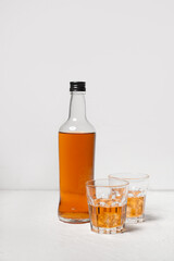 Bottle and glasses of rum with ice cubes on white background