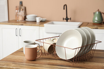 Holder with clean plates and cups on wooden table in kitchen