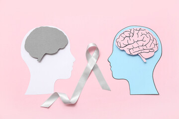 Paper human heads with brains and grey awareness ribbon on pink background. Cancer concept