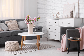 Sofa, armchair and coffee table with blooming magnolia branches in interior of living room