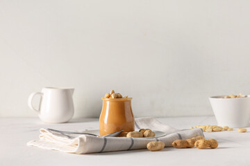 Jar of tasty peanut butter with spoon and nuts on white background