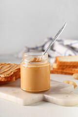 Jar of tasty peanut butter with spoon and toasts on white background