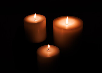 Three votive candles burning in a dark setting. Very moody romantic or religious feeling. Natural yellow and orange color.