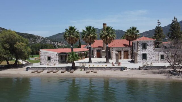 Tourist couple sunbathing in outdoor area of an isolated hotel property with private beach, Zaira hotel beautiful landscape surrounding hills and olive gardens, Lesvos Island, Drone shot