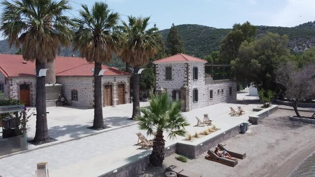 A female tourist reading a book sitting on outdoor lounging chair at a beachfront hotel property, Zaira Hotel, Mytilene, Lesvos Island, Drone shot