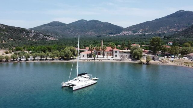 A luxury yacht sailing at seaport with Zaira hotel estate in view surrounded with olive trees garden and mountains, Mytilene, Lesvos Island, Establishing, Drone shot