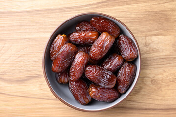 Date palm fruit (MedJool) in bowl on wooden background, Table top view