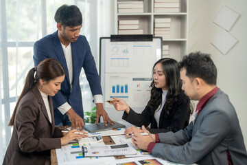 A group of people are sitting around a table with a white board behind them