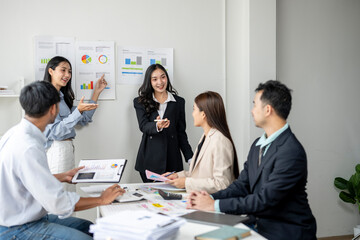 A group of people are gathered around a whiteboard with graphs and charts on it