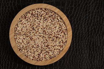 Top view of mixed quinoa grains in a bamboo plate on a textured black background, showcasing white, red, and black quinoa. Perfect for culinary and healthy food themes.