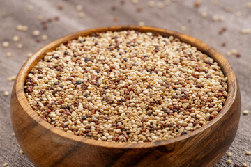 Wooden bowl filled with mixed quinoa grains, featuring white, red, and black seeds on a rustic wooden surface, ideal for healthy food and nutrition concepts.