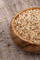 Rustic wooden bowl filled with mixed quinoa grains, featuring white, red, and black quinoa seeds on a textured wooden surface, perfect for healthy food concepts.