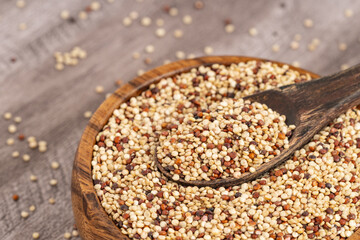 Mixed quinoa grains in a rustic wooden bowl with a spoon, featuring white, red, and black quinoa, ideal for healthy food and nutrition concepts.