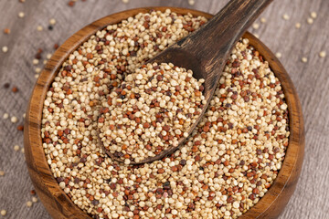 Mix of white, red and black quinoa seeds - Chenopodium quinoa. Top view of a wooden bowl filled with mixed quinoa grains and a wooden spoon, featuring white, red, and black quinoa, perfect for health 