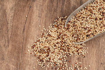 Mixed quinoa grains spilling from a metal scoop onto a wooden surface, showcasing red, white, and black seeds. Ideal for healthy eating and rustic food concepts.
