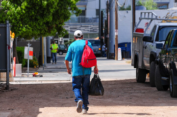 A pedestrian wearing a blue shirt and red backpack walks through an urban alley with construction...