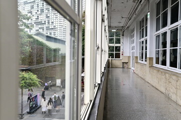 The corridor’s terrazzo flooring and window frame a striking cityscape. As people walk below, the view connects the calm indoor space with the dynamic movement outside.