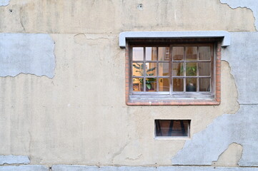 Against a timeworn wall with peeling paint, a red brick-framed glass window stands out. Inside, a...