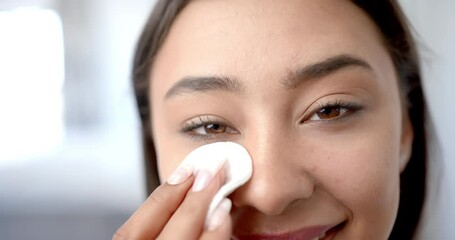 Smiling woman cleaning face with cotton pad, focusing on skincare routine