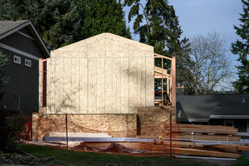 Large addition to residential house, construction in progress at framing stage with OSB, Oriented Strand Board, exterior wall installed on south end, sunny winter day job site
