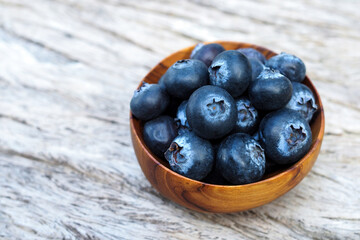 Blueberries in wood bowl on wooden table background.
