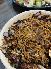 A bowl of jajangmyeon featuring chewy noodles coated in rich black bean sauce, topped with diced pork and vegetables. This iconic Korean-Chinese dish offers a savory and hearty flavor.
