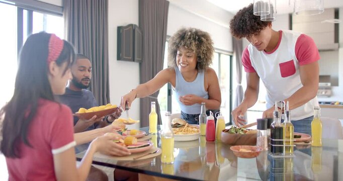 Diverse friends sharing food and drinks around dining table, enjoying time together