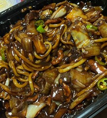 A bowl of jajangmyeon featuring chewy noodles coated in rich black bean sauce, topped with diced pork and vegetables. This iconic Korean-Chinese dish offers a savory and hearty flavor.
