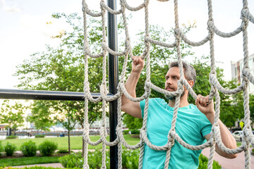 Man climbing net at obstacle course. Muscular man training at outdoor gym. Sport workout. Man sportsman do climbing exercise. Muscular strong athlete climbing net. Net climb. Copy space