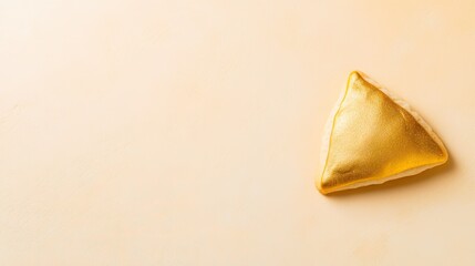 gold-painted hamantaschen cookie resting on matte pastel yellow surface with soft natural light